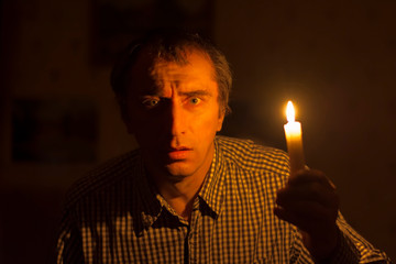 a man with a candle in his hand in a plaid shirt in a dark room