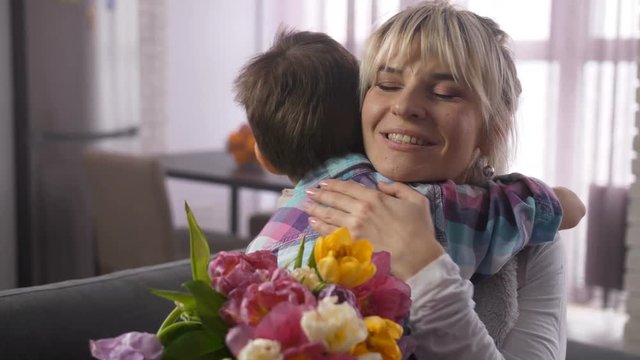 Close up cheerful mother holding bouquet of gorgeous multicolored tulip flowers hugging, kissing and stroking preadolescent son for beautiful flowers. Happy woman expressing graritude to beloved child