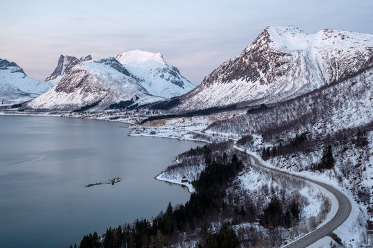 View over Senja at Bergsbotn in Winter with winding road towards range of snowy mountains, Troms, Norway