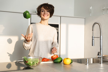 Happy young woman cooking fresh salad at the kitchen