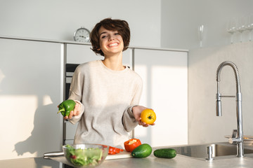 Happy young woman cooking fresh salad at the kitchen