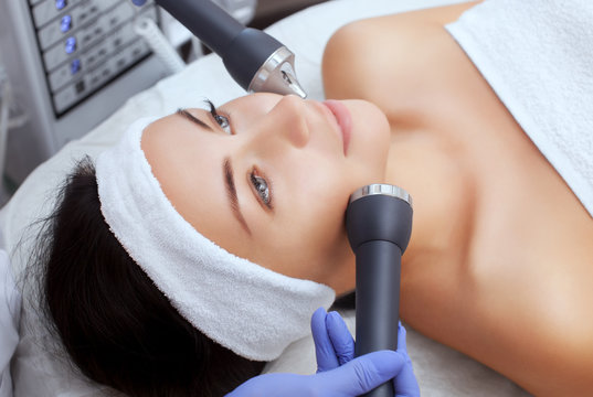 The cosmetologist makes the procedure an ultrasonic cleaning of the facial skin of a beautiful, young woman in a beauty salon.Cosmetology and professional skin care.