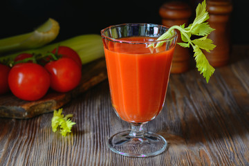 Fresh tomato juice in a glass goblet with a celery sprig and a tomato twig in the background in a low key