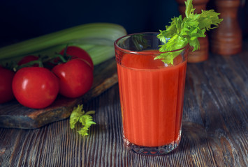 Fresh tomato juice in a glass goblet with a celery sprig and a tomato twig in the background in a low key