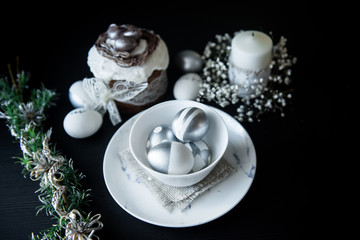 Traditional Easter cake with silver painted eggs, candles and willow on a black background. Selective focus