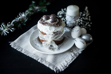 Traditional Easter cake with silver painted eggs, candles and willow on a black background. Selective focus