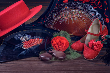 Beautiful and bright accessories for flamenco dance on a wooden background in a low key. Shawl, hat, fan, shoes, castanets and a flower for the hair.