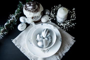Fototapeta premium Traditional Easter cake with silver painted eggs, candles and willow on a black background. Selective focus