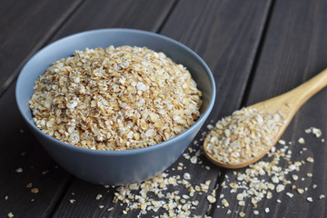 Rolled oats in bowl and spoon on dark wooden table