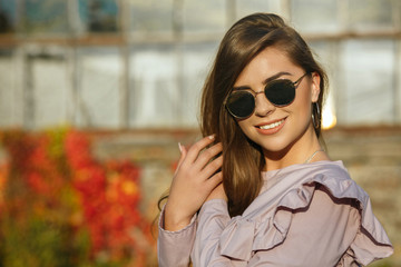 Smiling tanned model wearing trendy blouse and mirror glasses, posing outdoor with sun rays. Space for text