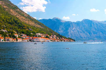 Incredible bright seascape. View of green wooded mountains and blue sea, blue sky and white clouds and a yacht sailing through the waves between the mountains. Boka Kotorska Bay, Montenegro