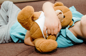 The boy is hugging a teddy bear in his hands. The child is lying on the bed holding a brown teddy bear, children's play.