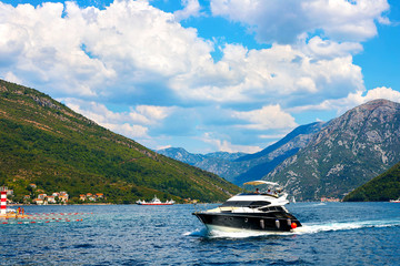 Fototapeta na wymiar Incredible bright seascape. View of green wooded mountains and blue sea, blue sky and white clouds and a yacht sailing through the waves between the mountains. Boka Kotorska Bay, Montenegro
