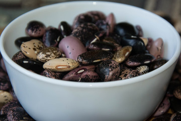 Close-up of colorful beans in porcelain bowl on a wooden table, haricot beans