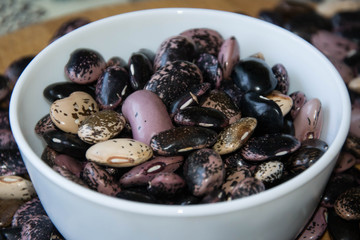 Close-up of colorful beans in porcelain bowl on a wooden table, haricot beans