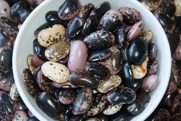 Close-up of colorful beans in porcelain bowl on a wooden table, haricot beans