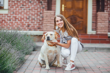 Young girl with retriever on walk in front of the house. Attractive woman stroking labrador retriever and looking into the camera.