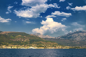 Fototapeta na wymiar Incredible bright seascape. View of green wooded mountains and blue sea, blue sky and white clouds. Boka Kotorska Bay, Montenegro