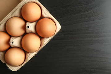 Chicken eggs in carton box on black background, space for text