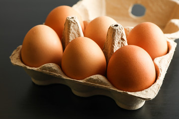 Chicken eggs in carton box on black background, space for text