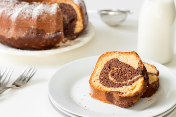 Marble bundt cake slaces on a white festive table set with milk and plates. Whole grain healthy rustic bakery.