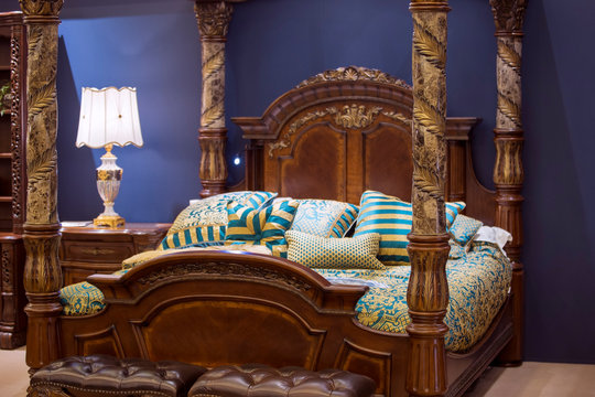 Huge bedroom in wooden style, carved chic wooden bed with columns and stoles, bedside tables and other furniture in the bedroom made in the same style with carved elements