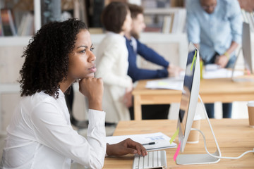 Serious black female employee thinking sitting in front of computer