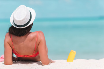 Beautiful young woman holding a suncream lying on tropical beach