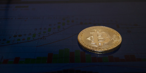 close up of one bitcoin over the monitor showing stock market chart