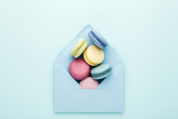 Colorful macarons in blue envelope on turquoise background. Top view, close up.