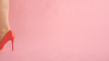Close-up of shapely female legs walking in sexy red high hells on coral background