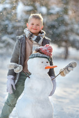 Smiling boy making cute snowman in the forest. Winter vacation