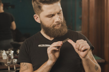 His professional tools. Professional barber checking his razor blade looking seriously