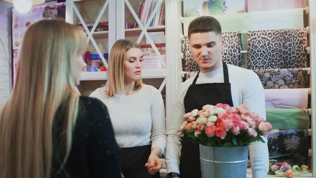 Young cheerful man and beautiful woman florists are talking to customer and giving advice