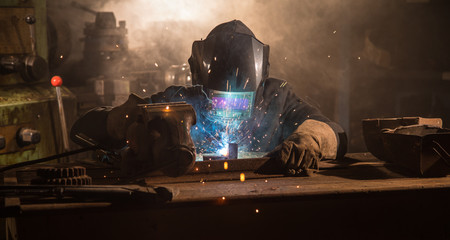 Welder is welding metal part in industrial workshop.