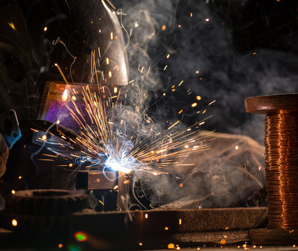 Welder is welding metal part in industrial workshop.