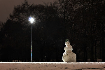lonely snowman under lantern in park by night