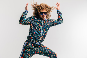 Excited adult funny man in stylish vintage clothes posing on white studio background. 80s fashion. Funky guy in tracksuit and sunglasses expressive indoor unusual portrait. Shouting cheerful male.