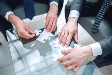close up.business people putting together a puzzle ,sitting behind a Desk