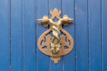 Close-up. Vintage handle for knocking on a blue wooden door in the form of two wriggling snakes.