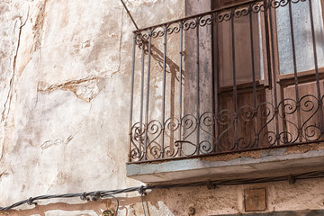 Old wall with peeling paint, scratched vintage plaster and a balcony with a rusty iron forged lattice.