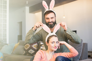 Young loving couple having fun with pink rabbit ears on head. Happy family preparing for Easter