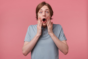 Close up of young man with blown away, amazed expression and dropped jaw isolated on pink...