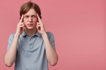 Close up young man thinking, trying hard to remember something looking focused to the rightside on blank copyspace, fingers on temples isolated pink background. Negative emotion facial expressions