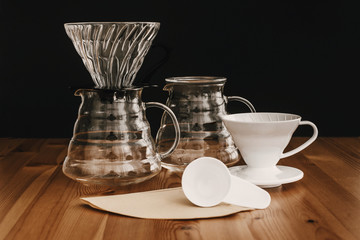 Glass flask, paper filters, glass and ceramic dripper, spoon for pour-over coffee. Alternative coffee brewing method. Stylish accessories and items for alternative coffee on wooden table