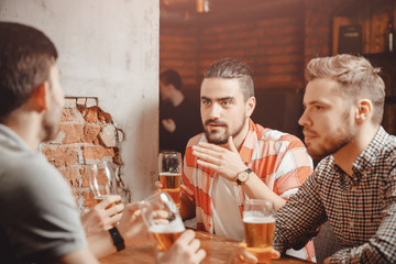 Friendly meeting. Guys drink beer at bar. Bearded man with pierced eyebrow tells interesting story, men listening