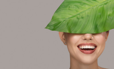 Woman smile and green leaf. Organic beauty. Gray background.