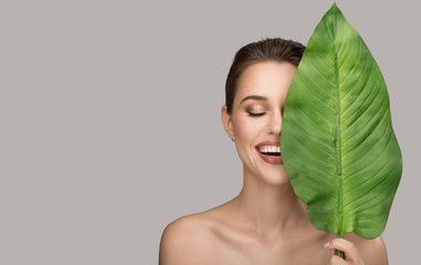 Portrait of woman and green leaf. Organic beauty. Gray background.