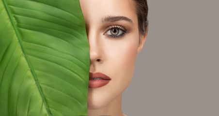 Portrait of woman and green leaf. Organic beauty. Gray background.