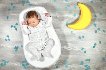 Newborn baby sleeps in a special orthopedic mattress Baby cocoon, on a wooden floor, toy moon and...
